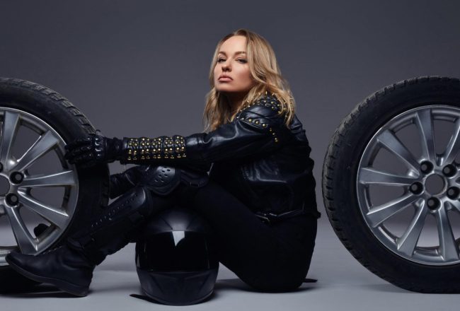 femme entre deux pneus de moto qui met un blouson moto noir en cuir clouté