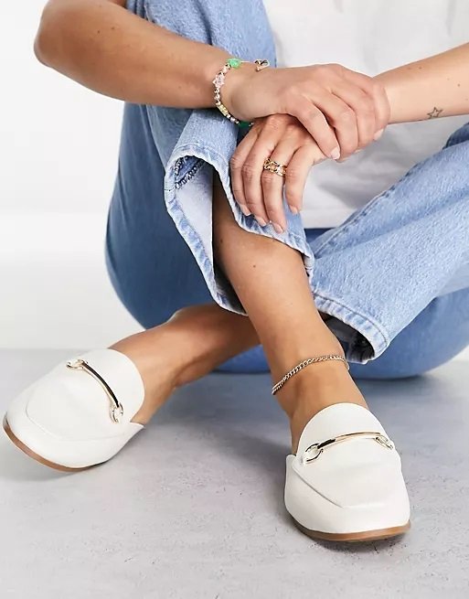 White open loafers with golden bits worn by a woman with tube jeans