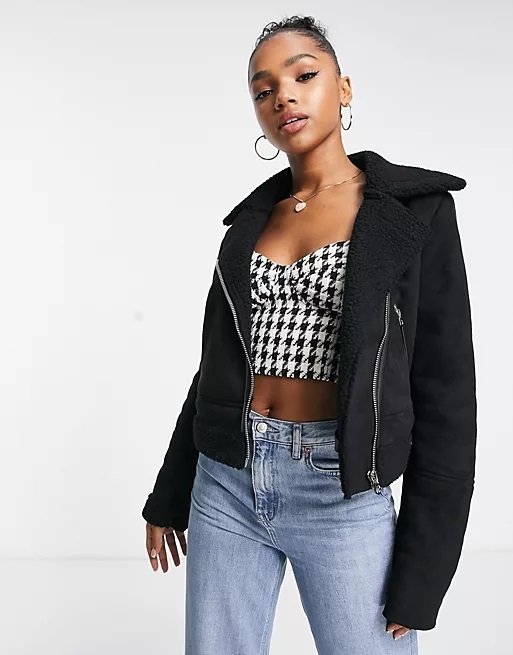 Woman wearing a black suede aviator jacket with a crop top and jeans