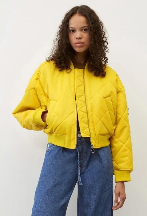 Woman wearing a yellow quilted bomber and tube jeans