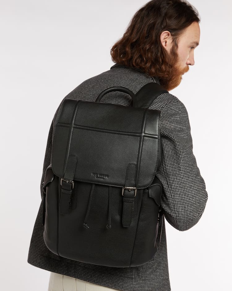 A bearded man wearing a leather backpack for work