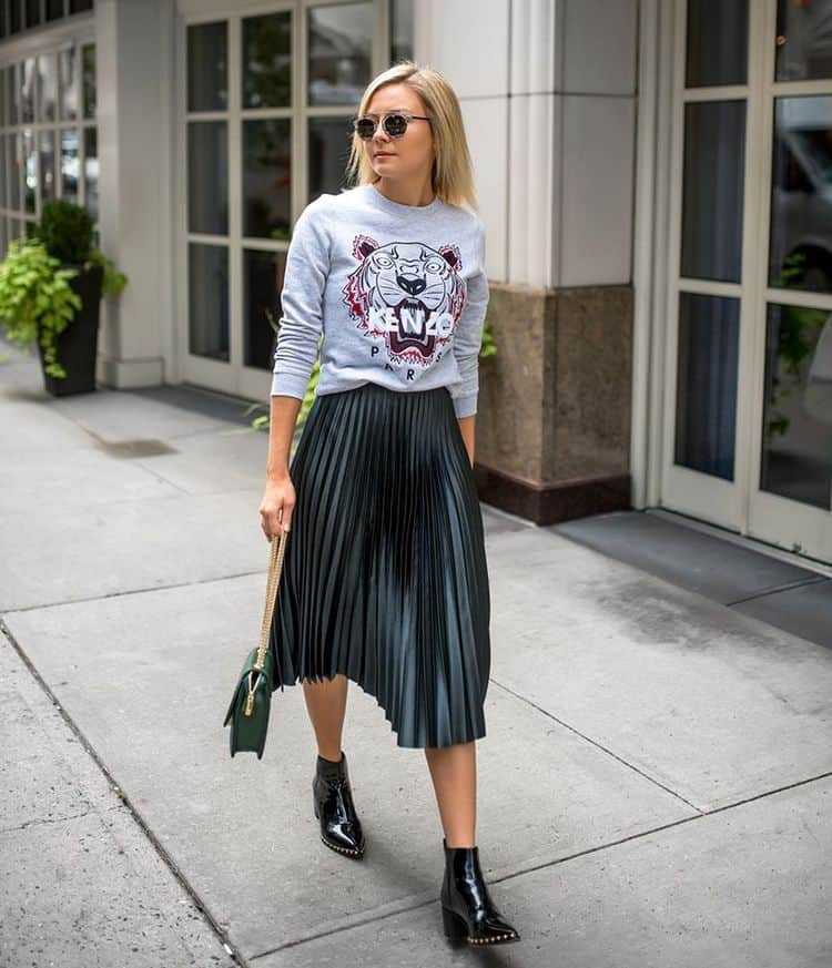 Woman wearing a gray sweatshirt with a pleated skirt and ankle boots