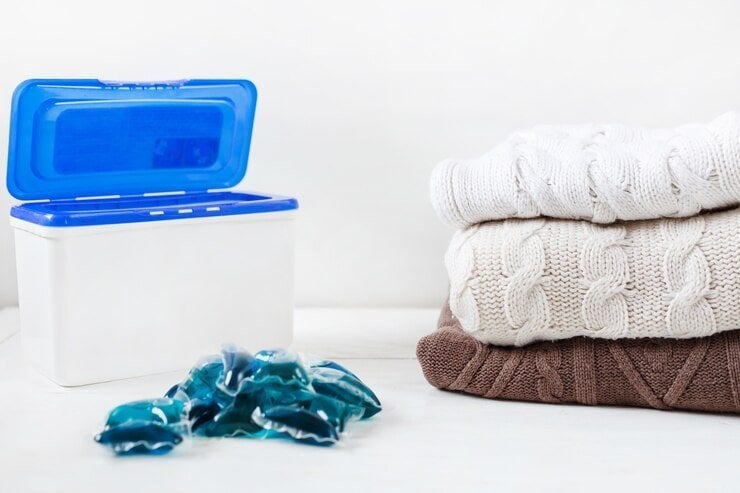 a pile of folded cardigans next to a detergent