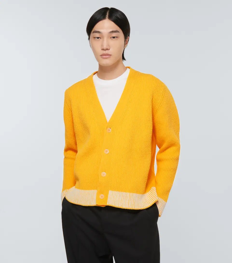 A man wearing a yellow cardigan, a t-shirt, and black pants